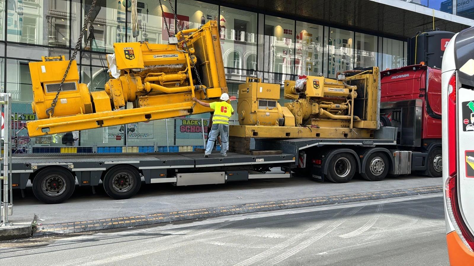 Deux groupes électrogènes Caterpillar chargés à la grue sur une semi-remorque porte-char, en centre-ville