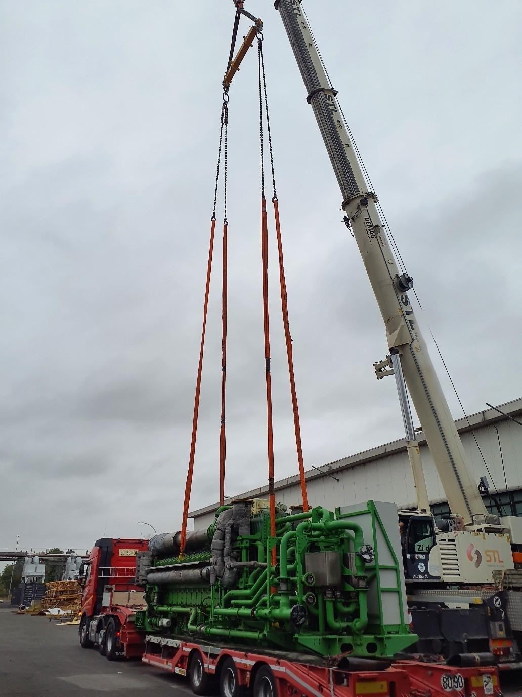 Grue mobile levant un moteur à gaz vert à l’aide d’un palonnier et de quatre élingues orange